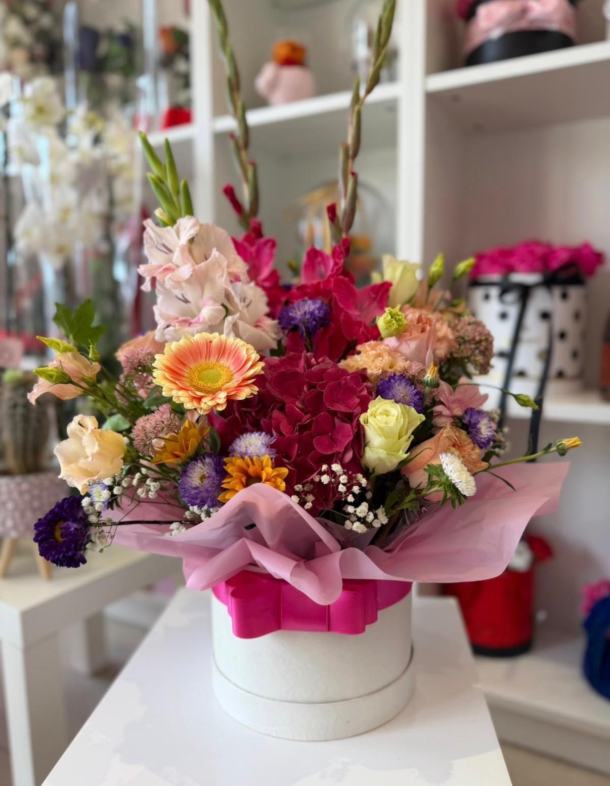 Spring bouquet of mixed garden flowers in a white box with a pink ribbon